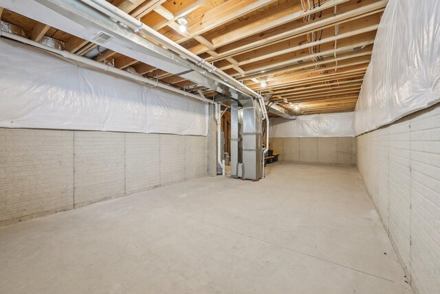 unfinished basement with visible vents, heating unit, and brick wall