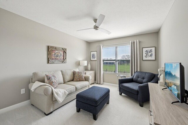 living area featuring baseboards, a ceiling fan, and light colored carpet