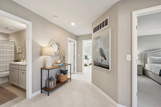 hall with baseboards, visible vents, and light carpet