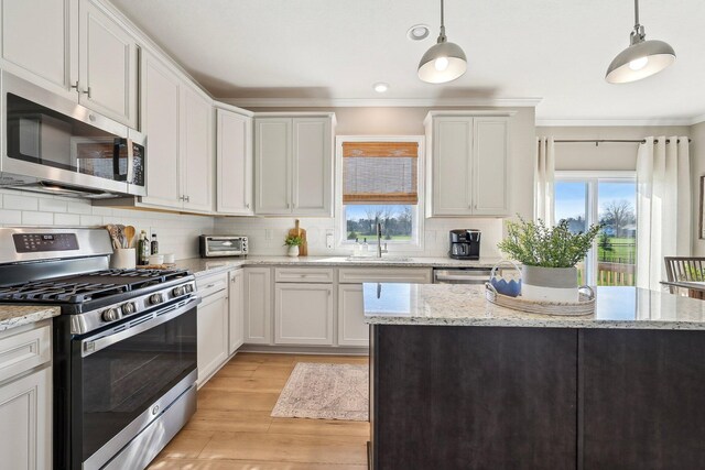 kitchen with crown molding, appliances with stainless steel finishes, a sink, light wood-style floors, and backsplash