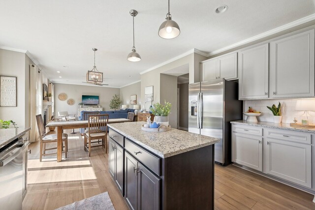 kitchen featuring appliances with stainless steel finishes, light wood finished floors, open floor plan, tasteful backsplash, and pendant lighting