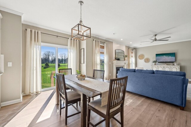dining area with crown molding, a fireplace, light wood-style flooring, ceiling fan with notable chandelier, and recessed lighting