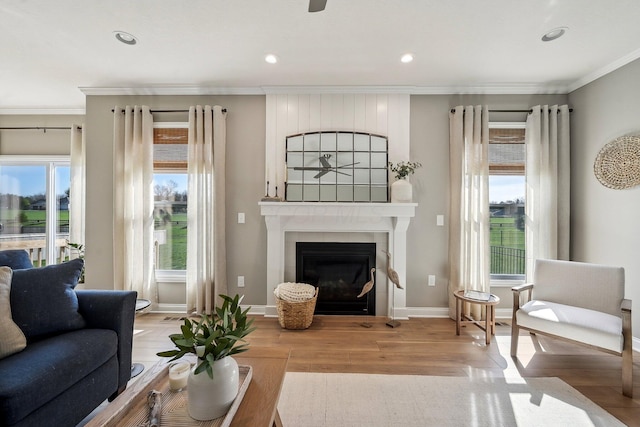 living room with baseboards, ornamental molding, a glass covered fireplace, and wood finished floors