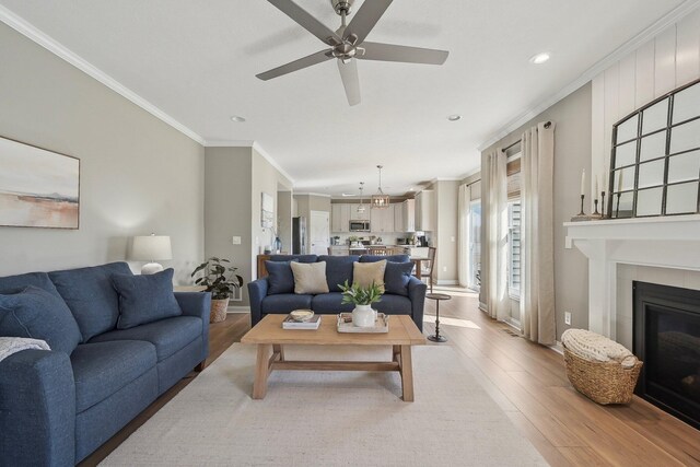 living room with crown molding, ceiling fan, recessed lighting, a tiled fireplace, and light wood finished floors