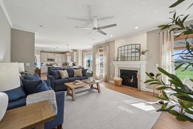 living room with ornamental molding, light wood finished floors, a ceiling fan, and a glass covered fireplace