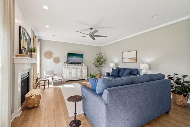 living area with a ceiling fan, ornamental molding, a glass covered fireplace, and wood finished floors
