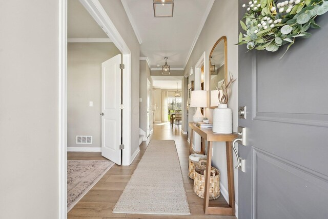 foyer featuring baseboards, visible vents, ornamental molding, and wood finished floors