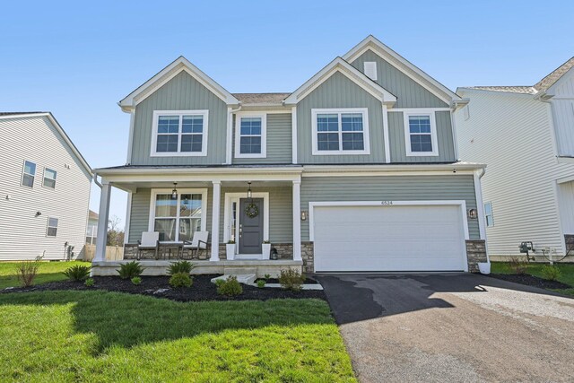 craftsman-style home featuring a porch, a front yard, driveway, and stone siding