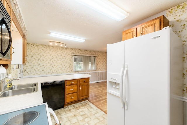 kitchen featuring brown cabinetry, a sink, light countertops, black appliances, and wallpapered walls