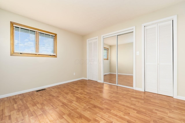 unfurnished bedroom featuring visible vents, light wood-style flooring, multiple closets, and baseboards