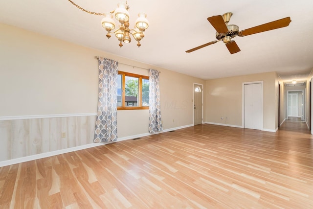 spare room featuring light wood-style floors, baseboards, and ceiling fan with notable chandelier