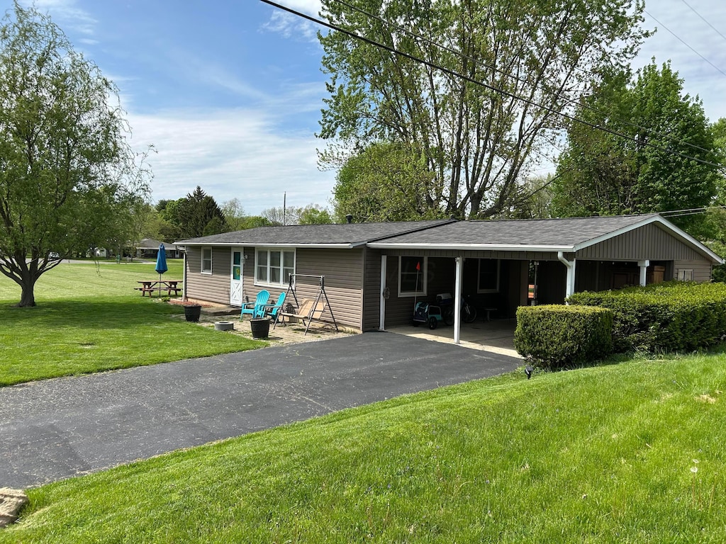 rear view of house with aphalt driveway, a yard, and a carport