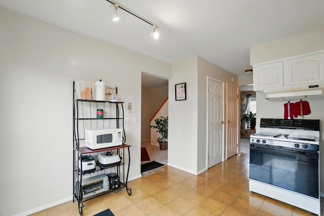kitchen featuring baseboards, white microwave, under cabinet range hood, white cabinetry, and range with gas stovetop