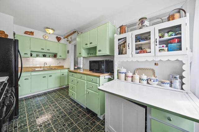 kitchen featuring a sink, green cabinets, open shelves, black microwave, and dark floors