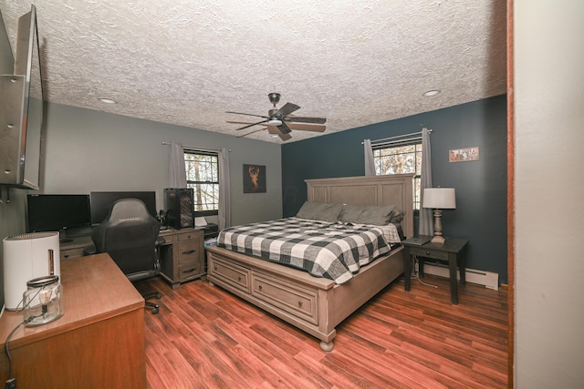 bedroom with a baseboard heating unit, a textured ceiling, ceiling fan, and wood finished floors