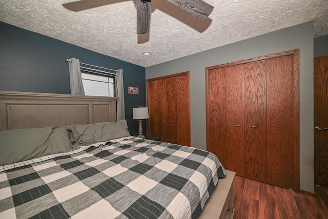 bedroom featuring a ceiling fan, two closets, a textured ceiling, and wood finished floors