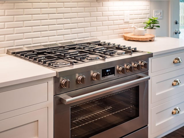 kitchen featuring stainless steel range, decorative backsplash, light countertops, and white cabinetry