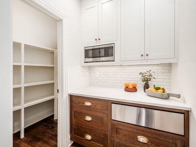 kitchen featuring stainless steel microwave, a warming drawer, white cabinetry, and decorative backsplash