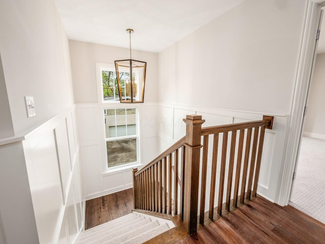 stairs with wood finished floors, wainscoting, a decorative wall, and a chandelier