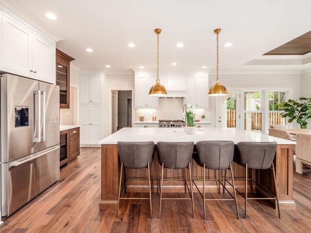 kitchen featuring high end fridge, tasteful backsplash, white cabinets, light countertops, and wood finished floors