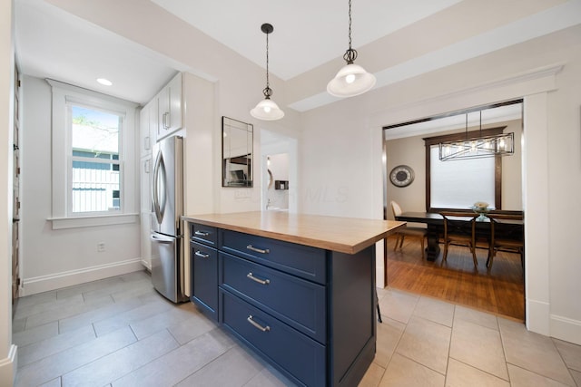 kitchen featuring light tile patterned flooring, butcher block countertops, freestanding refrigerator, baseboards, and blue cabinets