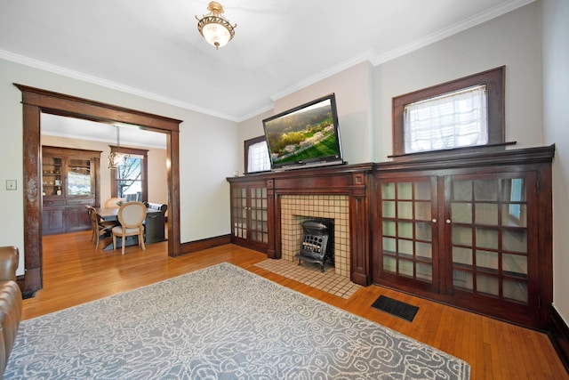 living area with visible vents, ornamental molding, wood finished floors, and a wood stove