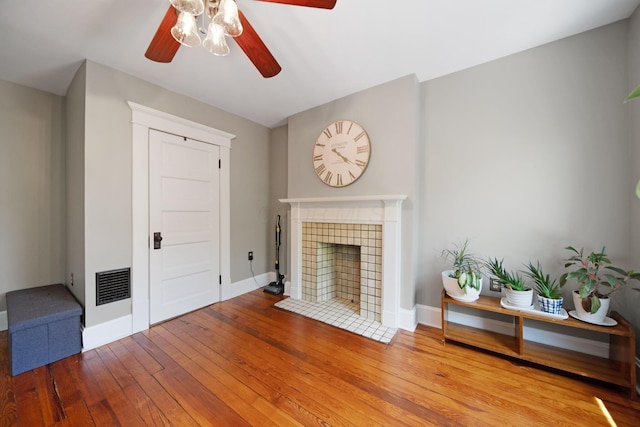 living room with visible vents, baseboards, ceiling fan, hardwood / wood-style flooring, and a tiled fireplace