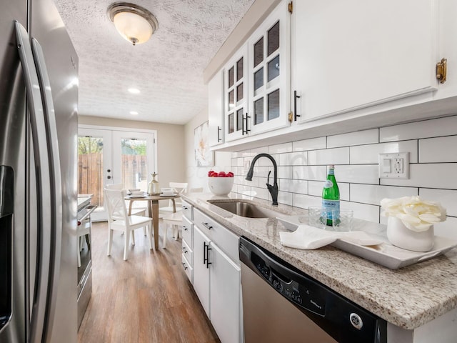 kitchen with a textured ceiling, white cabinets, a sink, appliances with stainless steel finishes, and wood finished floors