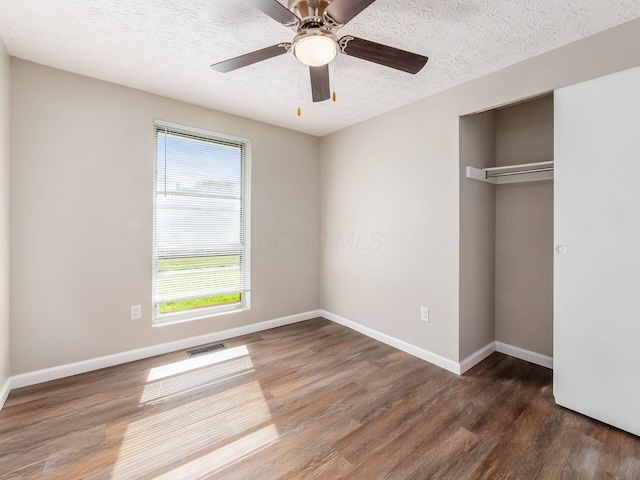 unfurnished bedroom featuring wood finished floors, visible vents, a textured ceiling, and multiple windows