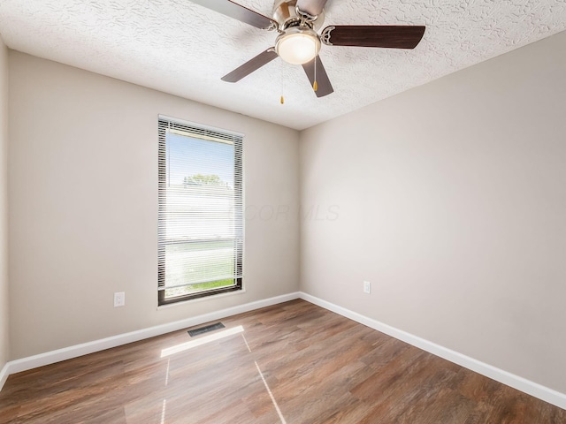 spare room featuring a ceiling fan, visible vents, wood finished floors, and baseboards