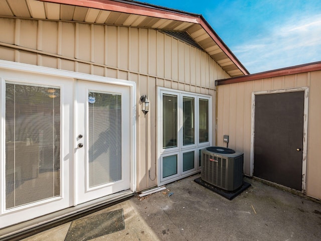 view of exterior entry with board and batten siding, central AC unit, and a patio area