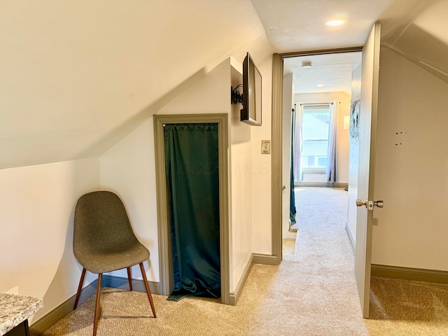 hallway with baseboards, light carpet, and vaulted ceiling