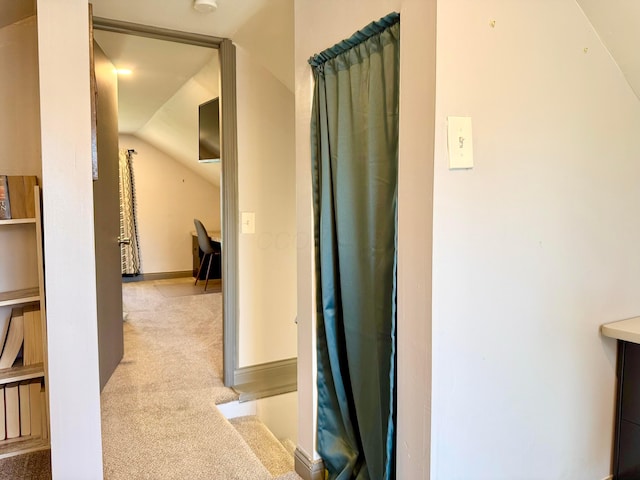 corridor featuring baseboards, carpet, and vaulted ceiling