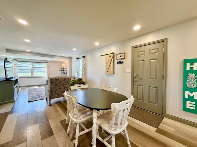 dining space with light wood finished floors, recessed lighting, a barn door, and baseboards