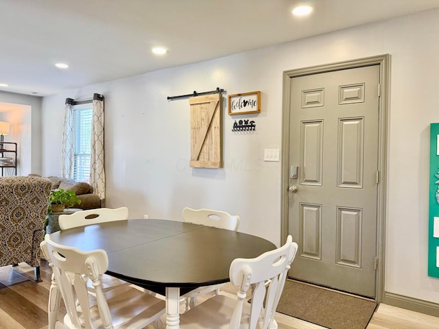 dining area with a barn door, light wood-style flooring, and recessed lighting