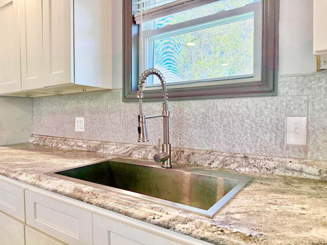 details with light stone countertops, a sink, white cabinetry, and decorative backsplash