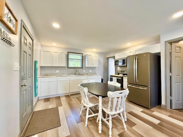 kitchen with stainless steel appliances, white cabinets, backsplash, light wood finished floors, and a sink