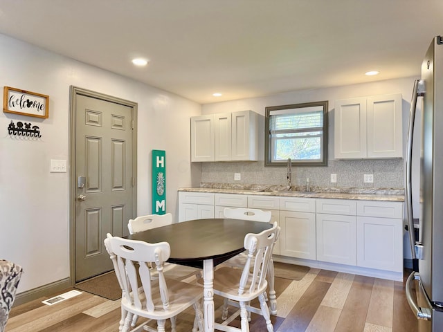 kitchen with freestanding refrigerator, white cabinetry, light wood finished floors, and a sink