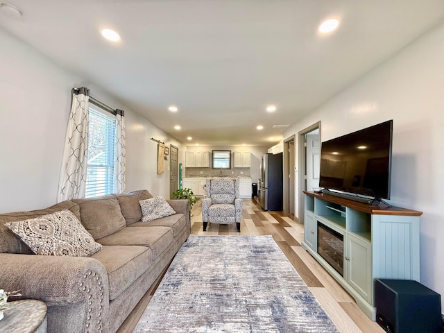 living room featuring recessed lighting, light wood-type flooring, and a glass covered fireplace