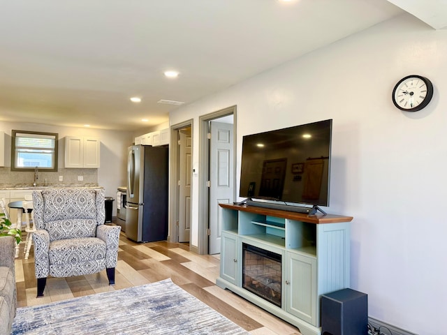 living area featuring recessed lighting, light wood finished floors, and a glass covered fireplace