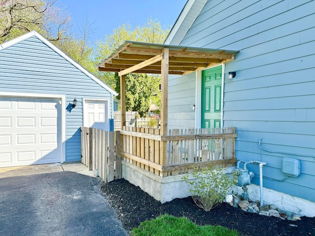 exterior space with fence, a detached garage, aphalt driveway, and an outbuilding