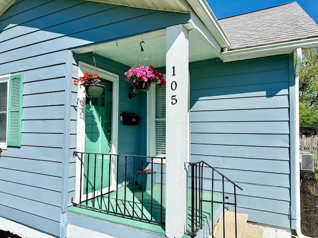 doorway to property featuring cooling unit and a shingled roof
