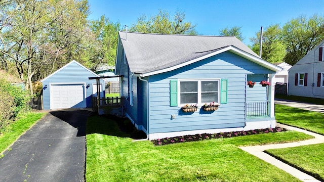 exterior space with a front yard, an outbuilding, aphalt driveway, a detached garage, and roof with shingles