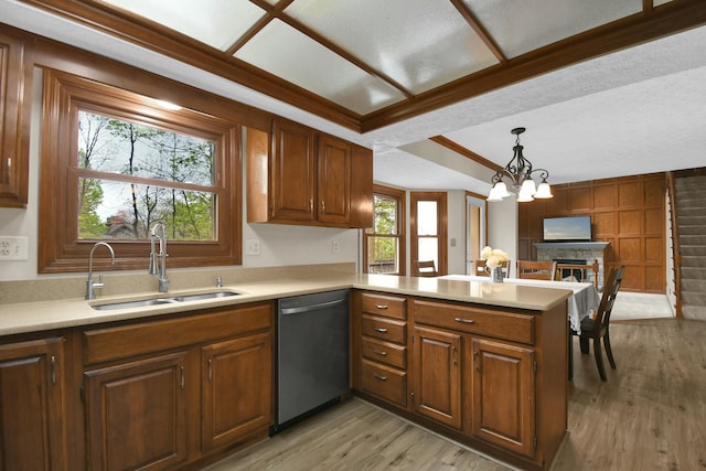 kitchen featuring a sink, dishwasher, light countertops, light wood-style flooring, and a peninsula