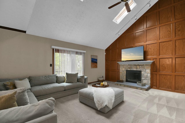 carpeted living room with track lighting, a fireplace, ceiling fan, high vaulted ceiling, and a skylight