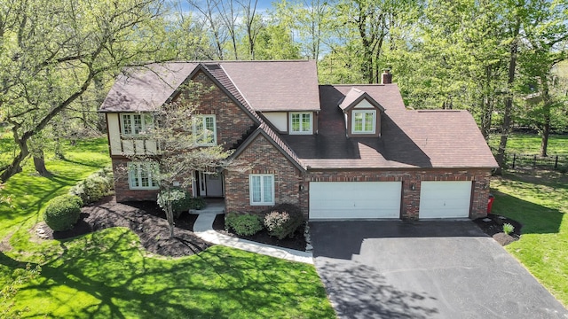 view of front facade featuring fence, brick siding, aphalt driveway, a front yard, and a chimney