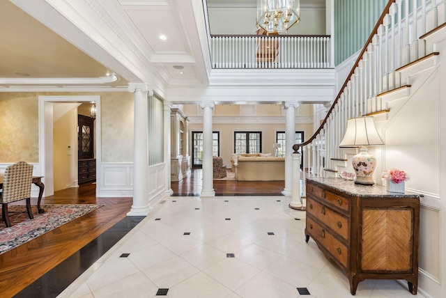 entryway with an inviting chandelier, ornamental molding, decorative columns, stairway, and a wainscoted wall