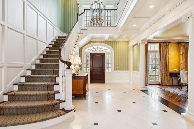 foyer entrance featuring a towering ceiling, crown molding, stairway, a chandelier, and a decorative wall