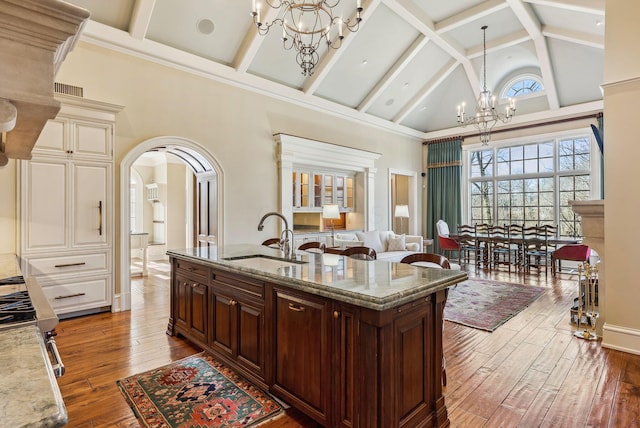 kitchen with dark wood-style floors, high vaulted ceiling, arched walkways, a sink, and a notable chandelier