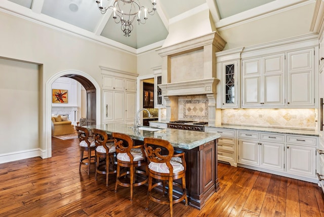 kitchen featuring light stone counters, a sink, arched walkways, a kitchen bar, and glass insert cabinets